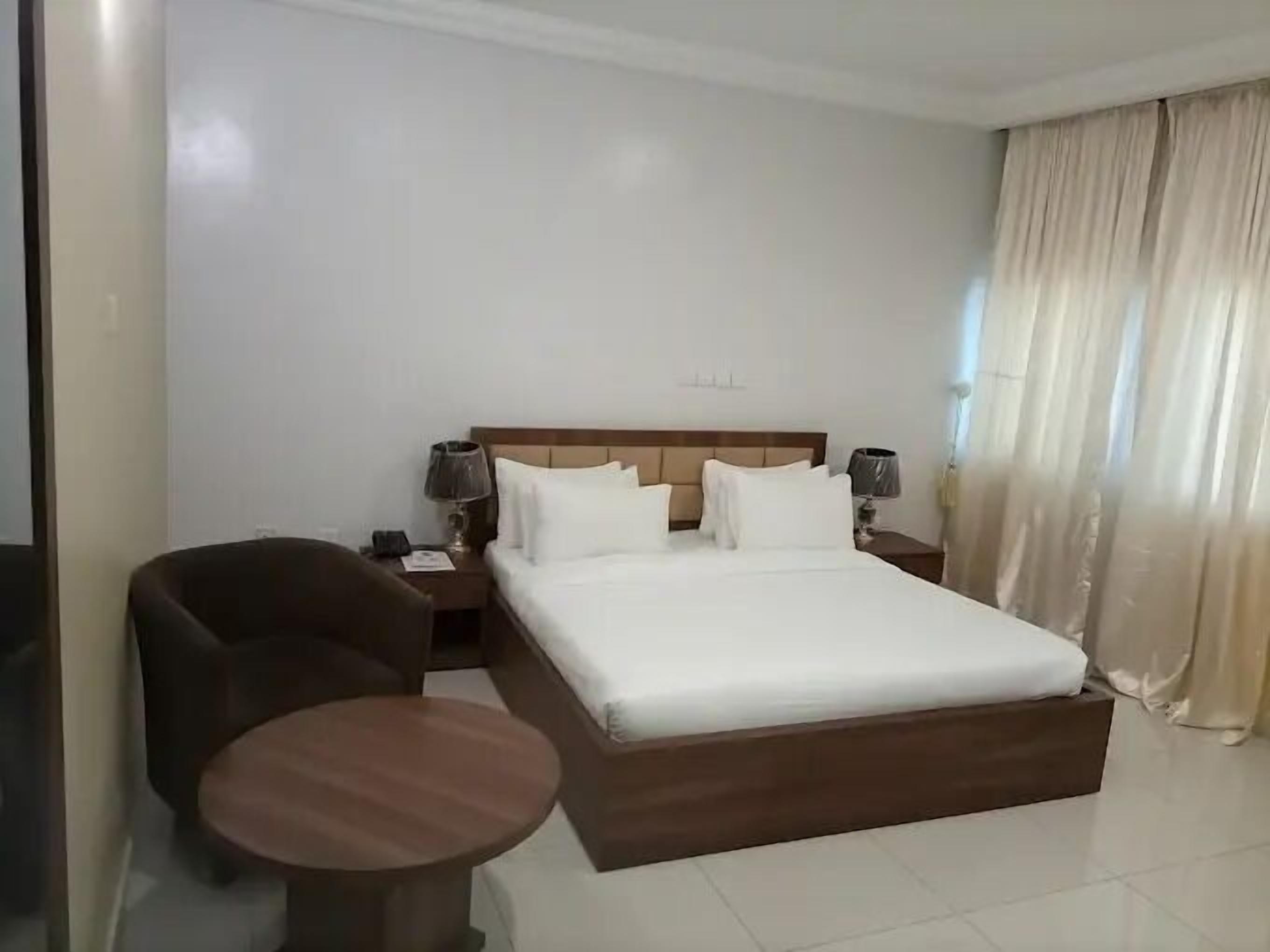 Une chambre d’hôtel avec un grand lit, deux tables de chevet avec des lampes, une petite table ronde et une chaise.