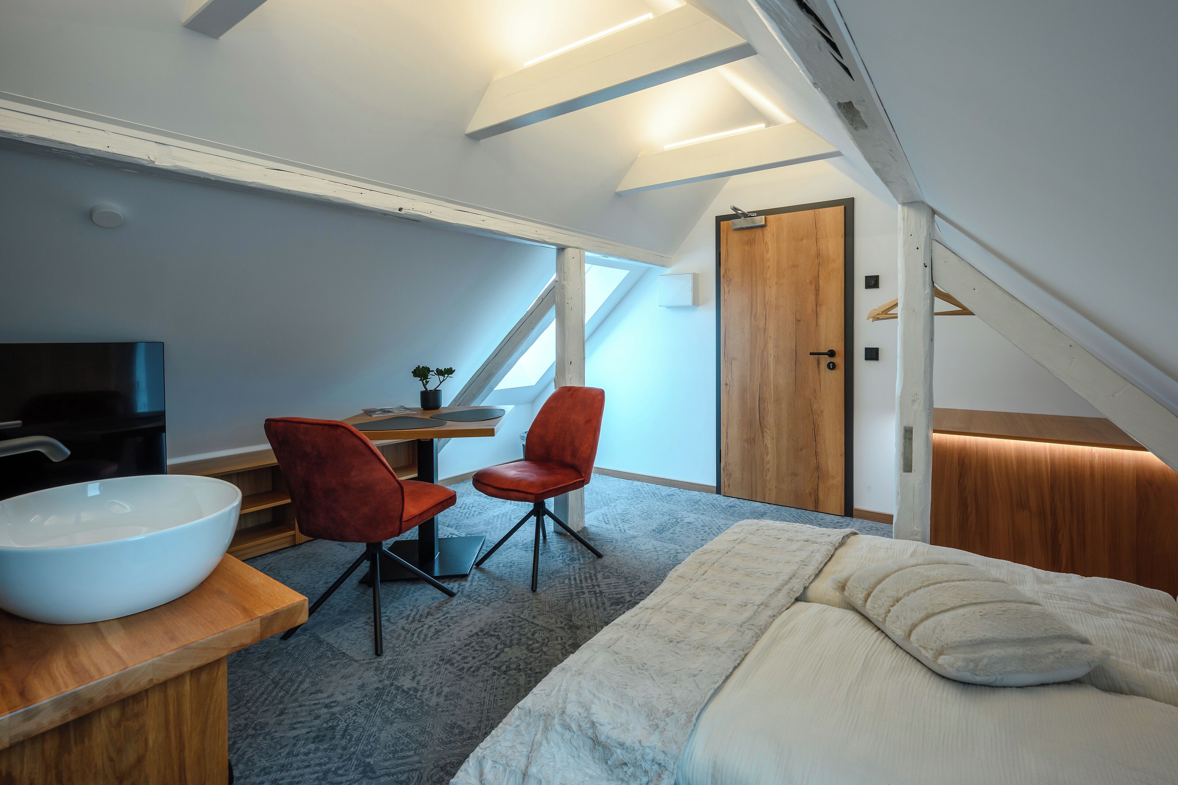 Una camera da letto moderna con un letto grande, una scrivania in legno, due sedie rosse, una ciotola bianca sulla scrivania e un lucernario.