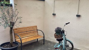 A wooden bench, a potted plant, and a bicycle in an outdoor area with a tiled floor and a pergola overhead. - Pension Domquartier Naumburg (Naumburg)
