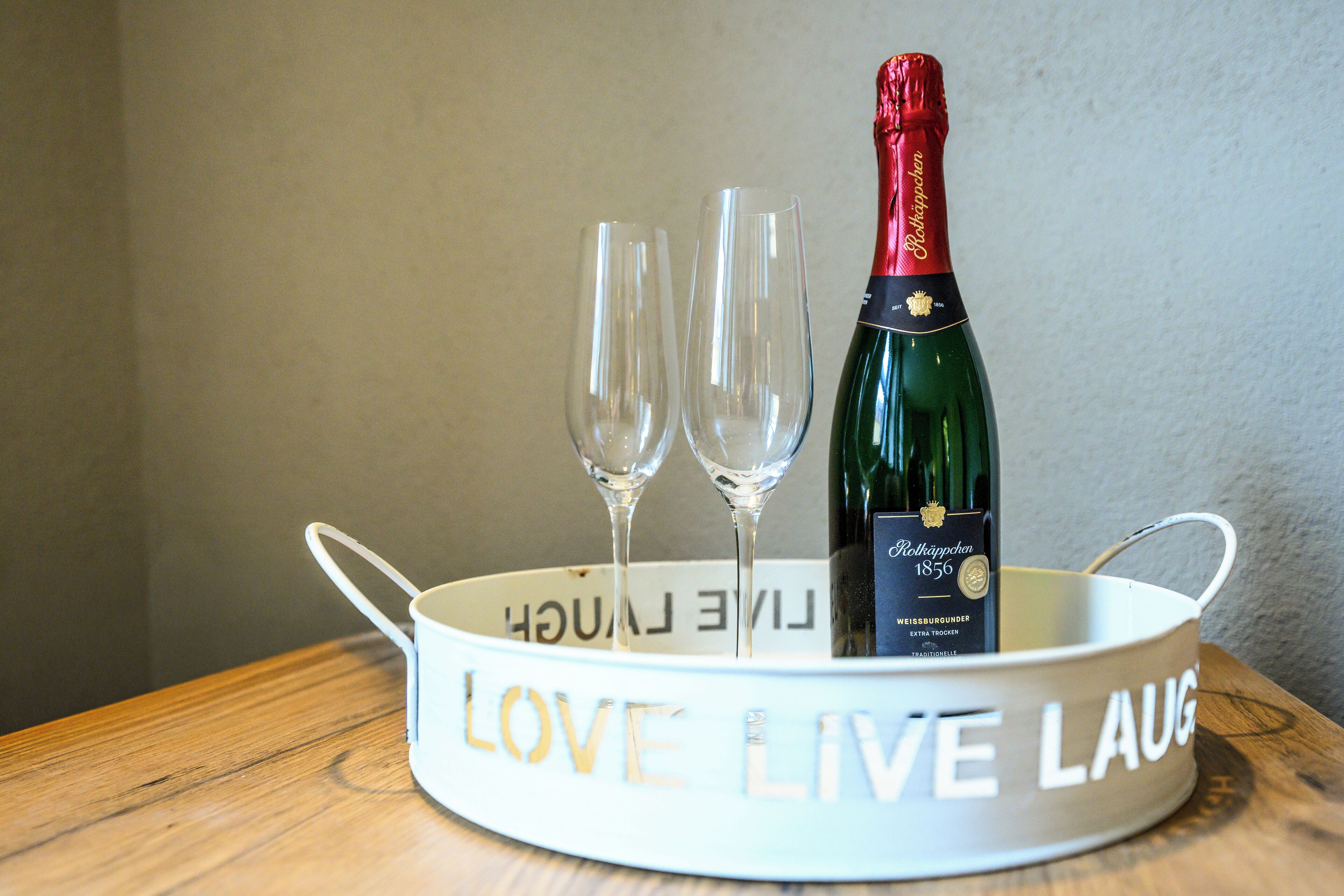 A bottle of Rothäppchen 1856 wine with two empty glasses in a white container with 'LOVE LIVE LAUGH' text.