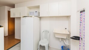 A compact kitchen with white cabinets, a refrigerator, a microwave, a sink, and a chair. - Cozy and practical apartment in a residential neighborhood (Palhoça)