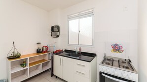 A compact kitchen with white cabinets, a black countertop, a gas stove, and a window above the sink. - Cozy and practical apartment in a residential neighborhood (Palhoça)