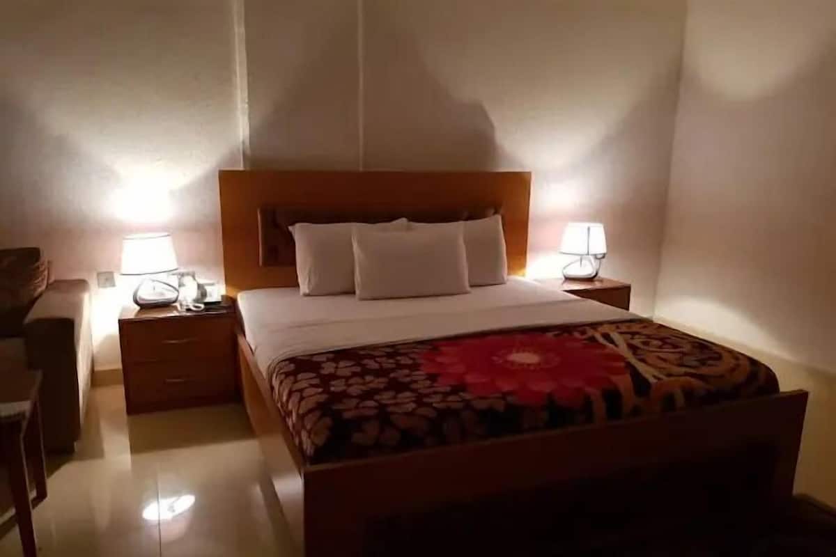 A hotel room with a wooden bed, two bedside tables with lamps, a small desk, and a chair.