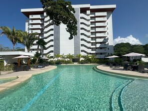 Un hôtel moderne doté d’une piscine centrale, entourée d’espaces de détente et de palmiers.
