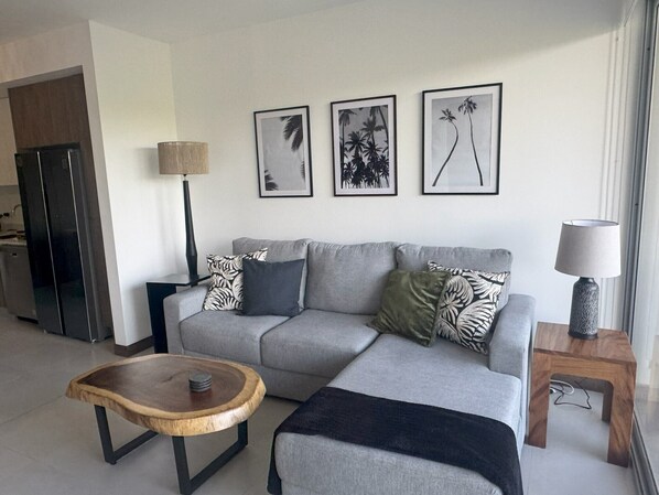 Un salon moderne avec un canapé gris, une table basse en bois et une table d’appoint avec une lampe. Trois tableaux encadrés ornent le mur.