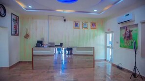 A reception area with a polished floor, a desk with computers, framed pictures on the wall, and an air conditioning unit. - MTown Hotel and Suites  (Dutse)