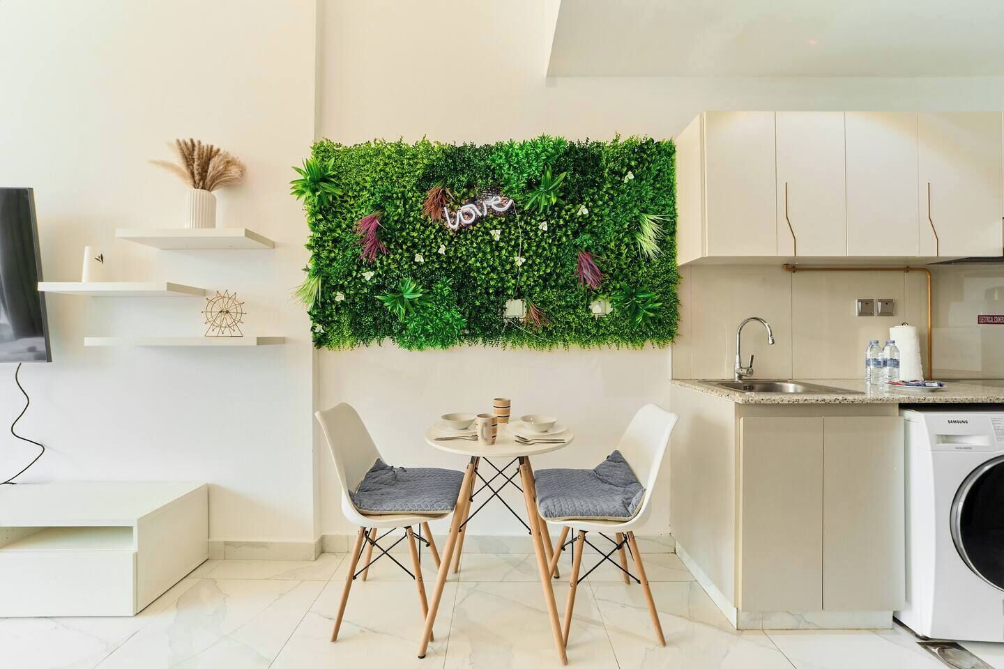 A modern kitchen with a green wall decor, a dining area with two chairs, and a washing machine.