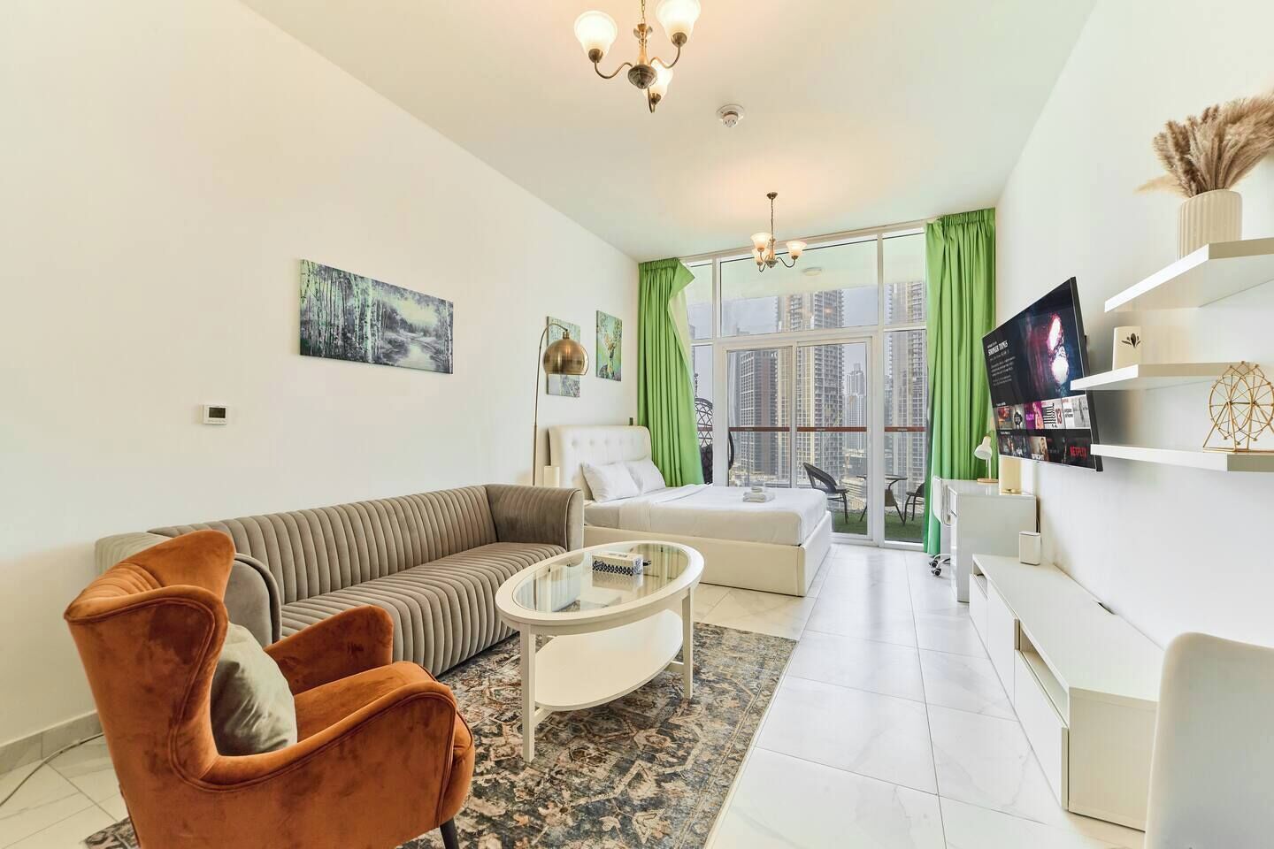Un salon moderne avec un canapé, un fauteuil et une table basse. Un téléviseur est fixé au mur, et il y a une fenêtre avec des rideaux.