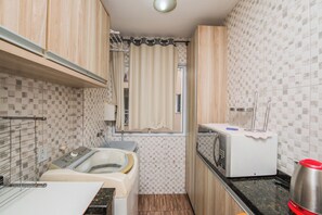Une cuisine compacte équipée d’un lave-linge intégré, d’un four à micro-ondes et d’un petit plan de travail.