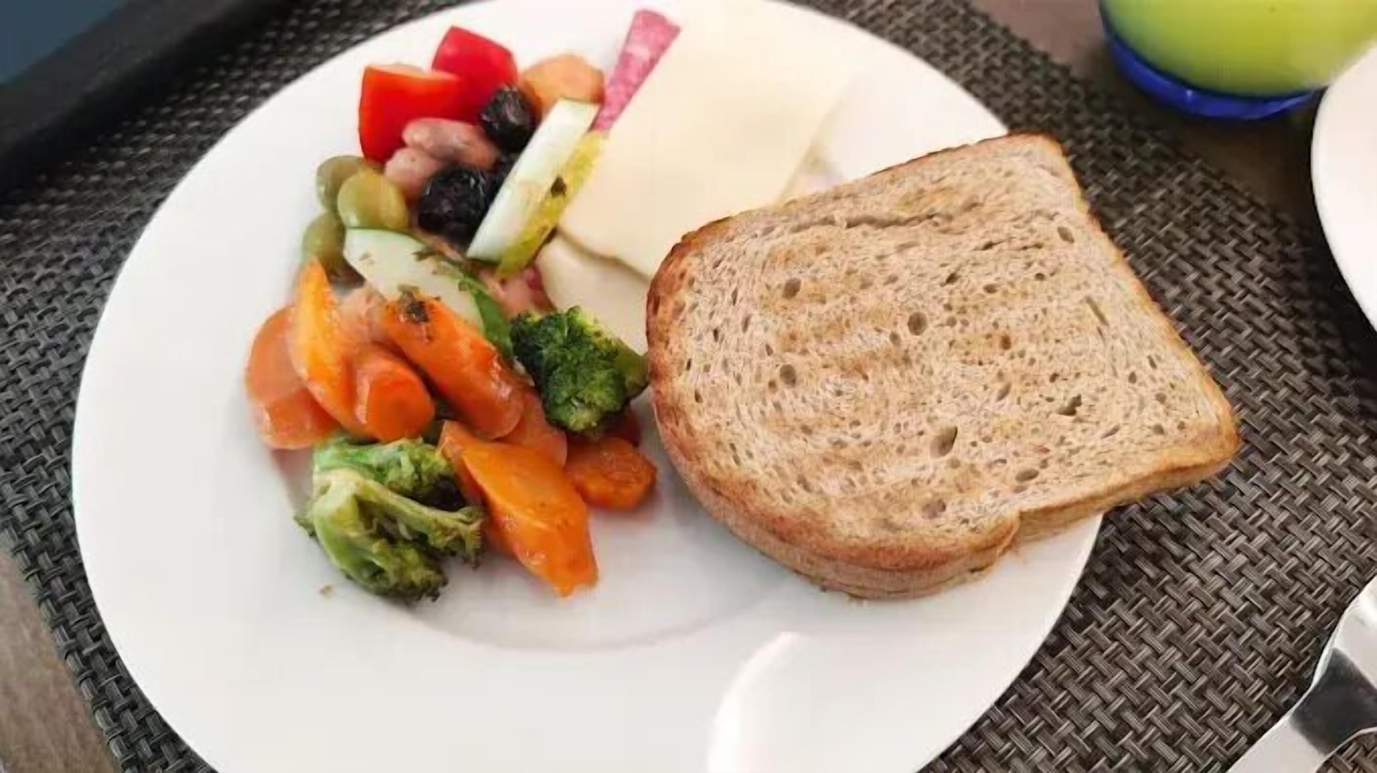 A plate with a slice of bread, mixed vegetables, and a piece of cheese.
