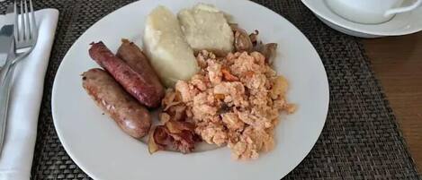 A breakfast plate with sausages, mashed potatoes, and scrambled eggs on a woven placemat.