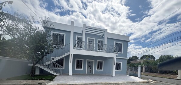 A two-story building with a balcony, a staircase, and a gated entrance. - Cozy 2-bedroom apartment in serene Bonao Dominican Republic with AC (Bonao)