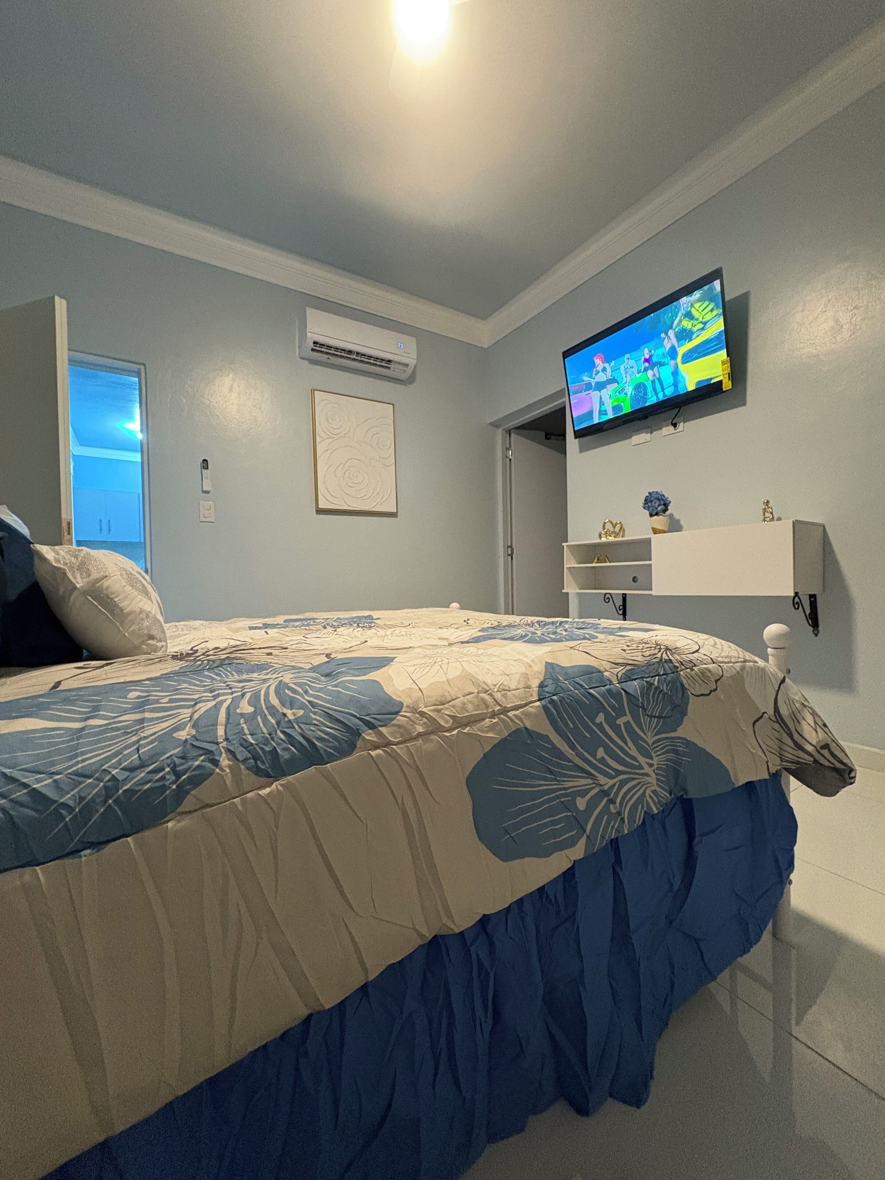 A bedroom with a bed, a television mounted on the wall, and a door leading to another room.