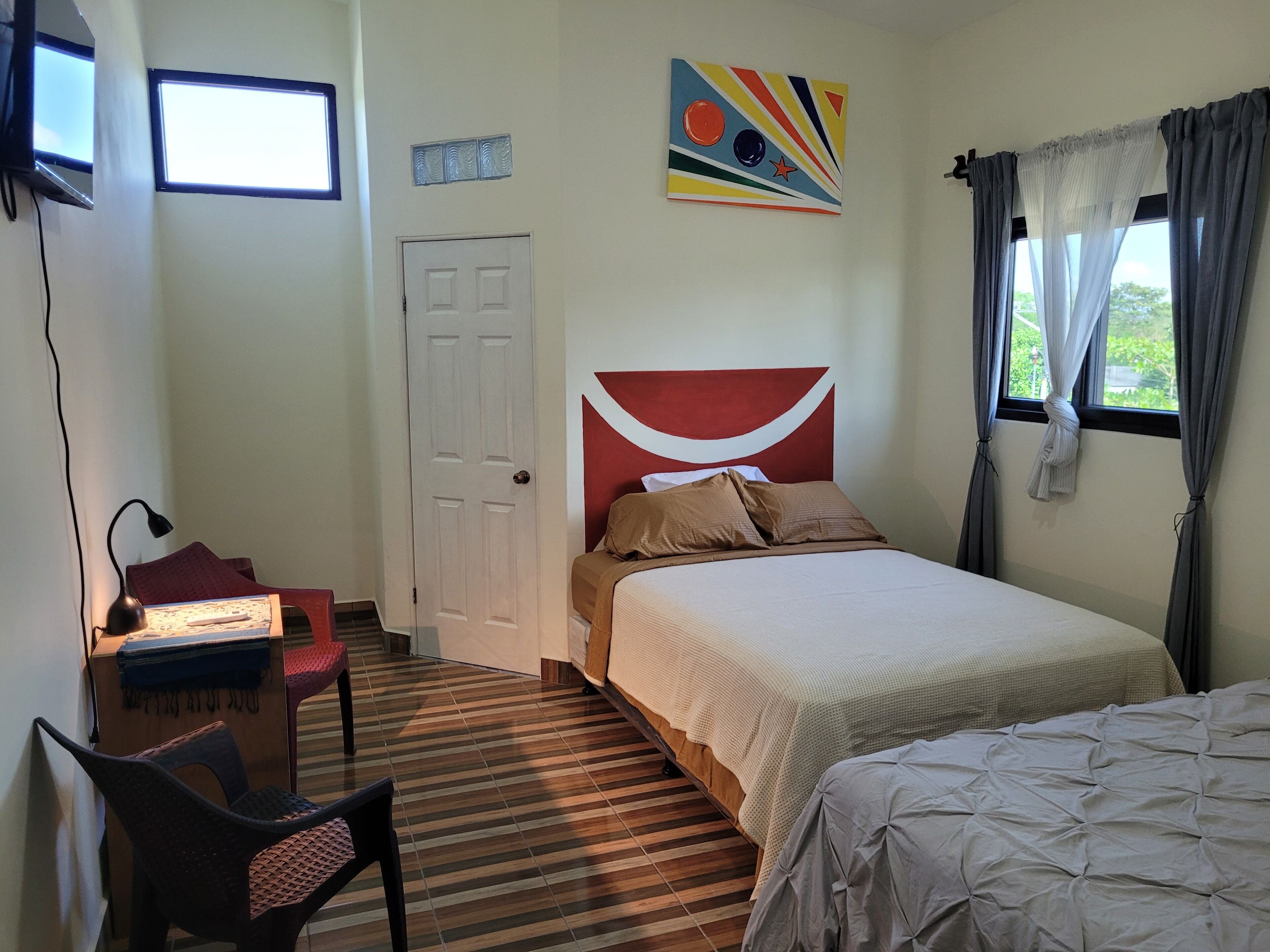 A bedroom with a bed, a desk with a chair, a window with curtains, and a door.