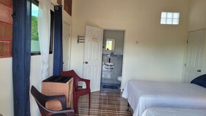 A compact hotel room with two beds, a small desk, a chair, a bathroom with a sink and toilet, and a window with curtains. - Luxury posada inn (Los Amates)