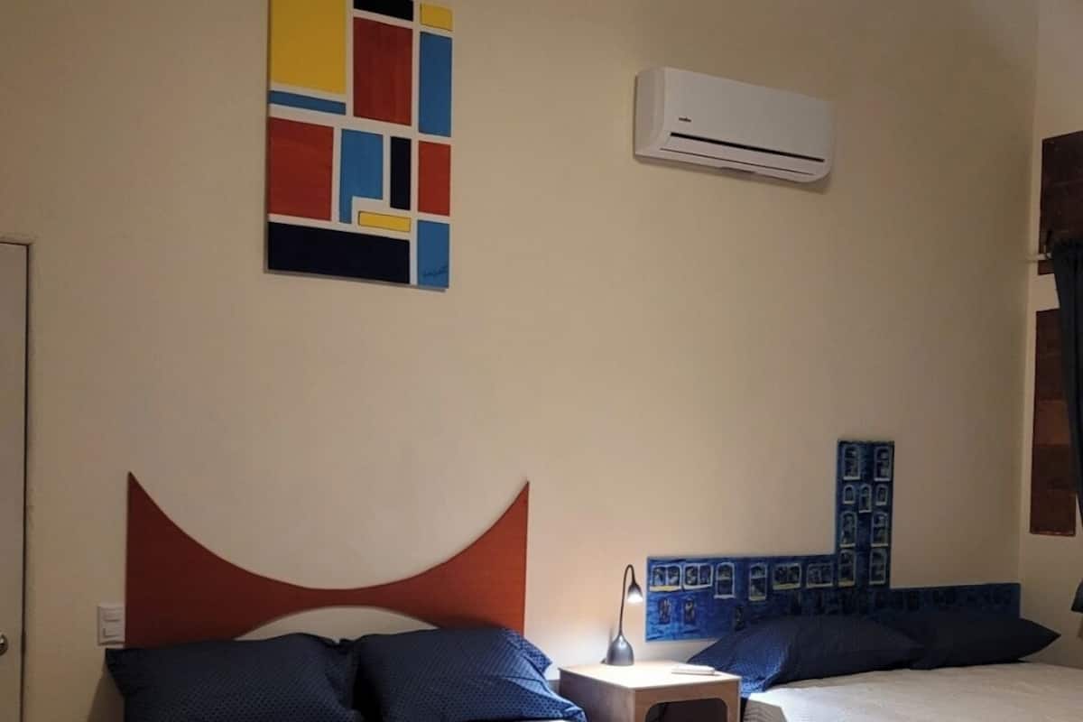 A hotel room with two beds, a ceiling fan, an air conditioner, and a wall art piece.