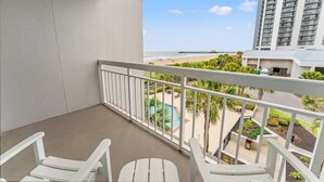 Een balkon met witte stoelen, een zwembad en uitzicht op het strand en hoge gebouwen.