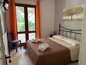 Een slaapkamer met een bed, een stoel, een schilderij en uitzicht door een raam.