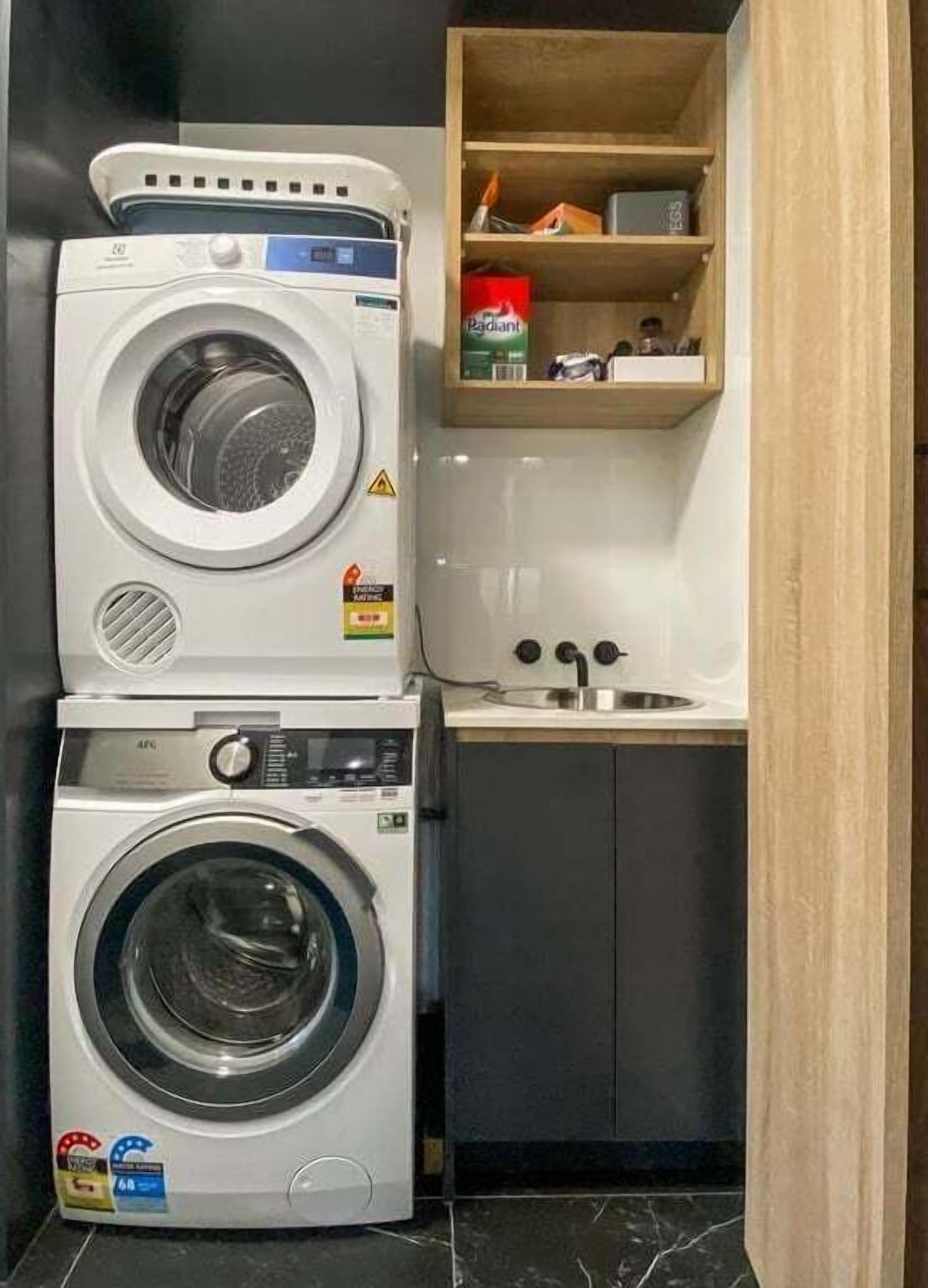 A compact laundry area with stacked washers and dryers, a small shelf with cleaning supplies, and a sink.