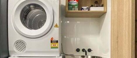 A compact laundry area with stacked washers and dryers, a small shelf with cleaning supplies, and a sink.