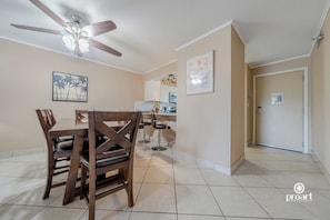 A dining area with a wooden table and chairs, a ceiling fan, and a kitchen in the background.