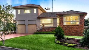 A two-story house with a garage, a front yard with a lawn and a small tree, and a brick exterior. - Luxury room + Pool + Ensuite (Bradbury)