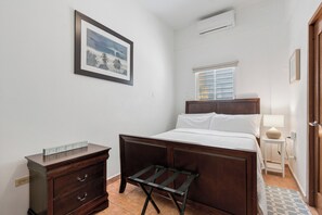 A bedroom with a bed, a bedside table, a nightstand, a dresser, a window with blinds, an air conditioning unit, and a framed picture on the wall. - Eco friendly beachfront oasis (Rincón)
