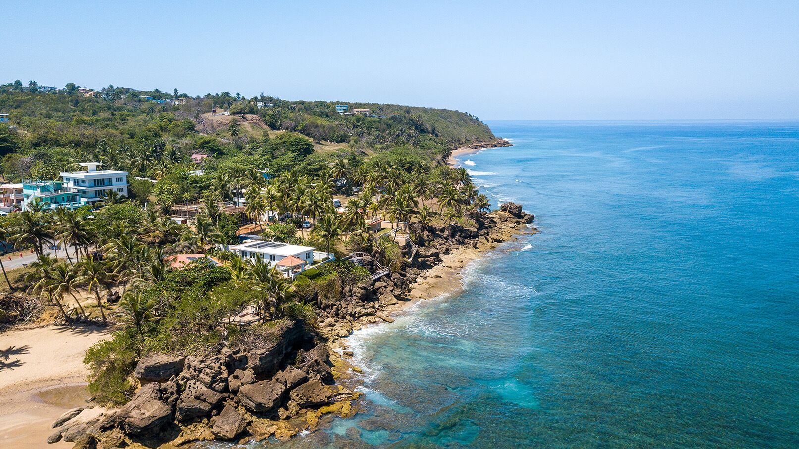 A coastal area with residential buildings, a beach, and rocky terrain.