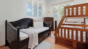 A bedroom with a bed, a wooden chair, a nightstand, and a window with shutters. - Eco friendly beachfront oasis (Rincón)