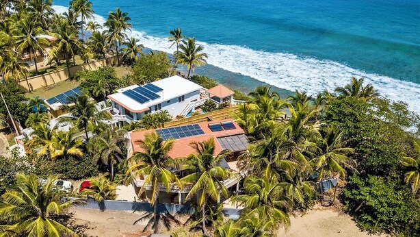 A coastal property with multiple buildings, including a house with solar panels, surrounded by palm trees and a beach. - Eco friendly beachfront oasis (Rincón)