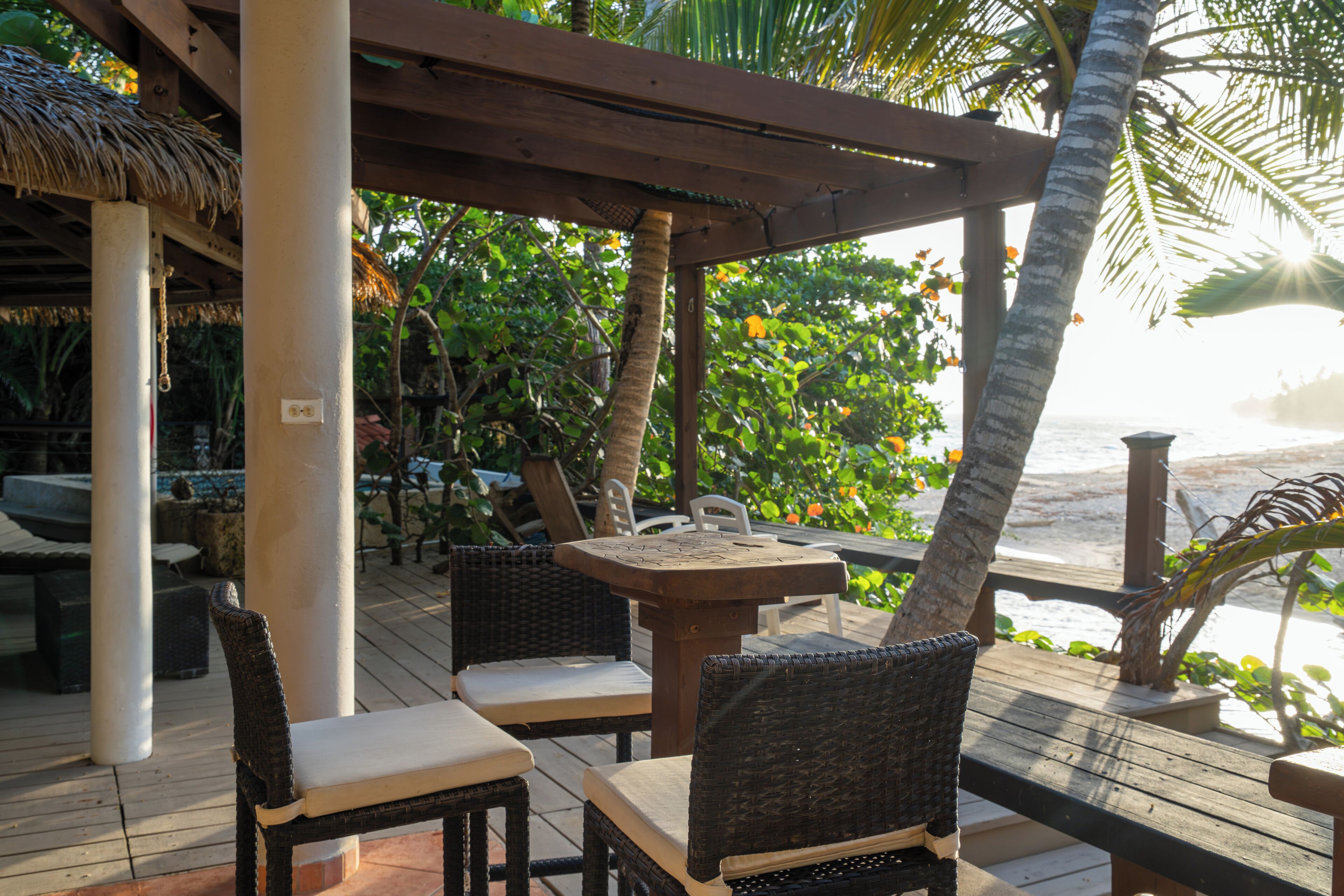 An outdoor seating area with wicker chairs and a wooden table, overlooking a beach.