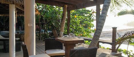 An outdoor seating area with wicker chairs and a wooden table, overlooking a beach.