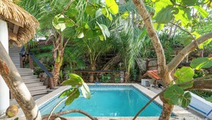 A swimming pool surrounded by tropical vegetation, a wooden staircase, and a thatched-roof structure. - Eco friendly beachfront oasis (Rincón)
