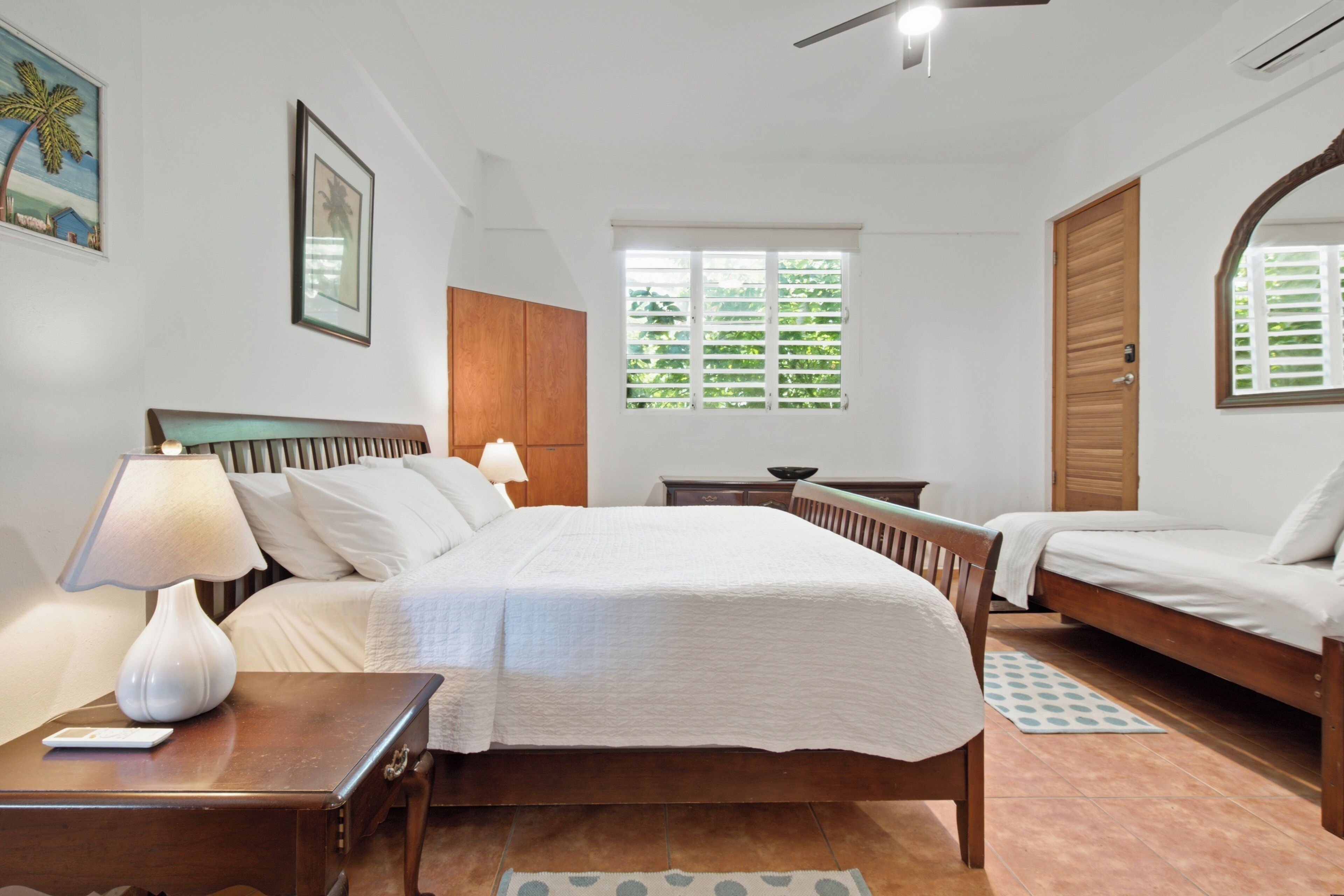 A bedroom with a bed, bedside tables, a lamp, a window with blinds, and a door.