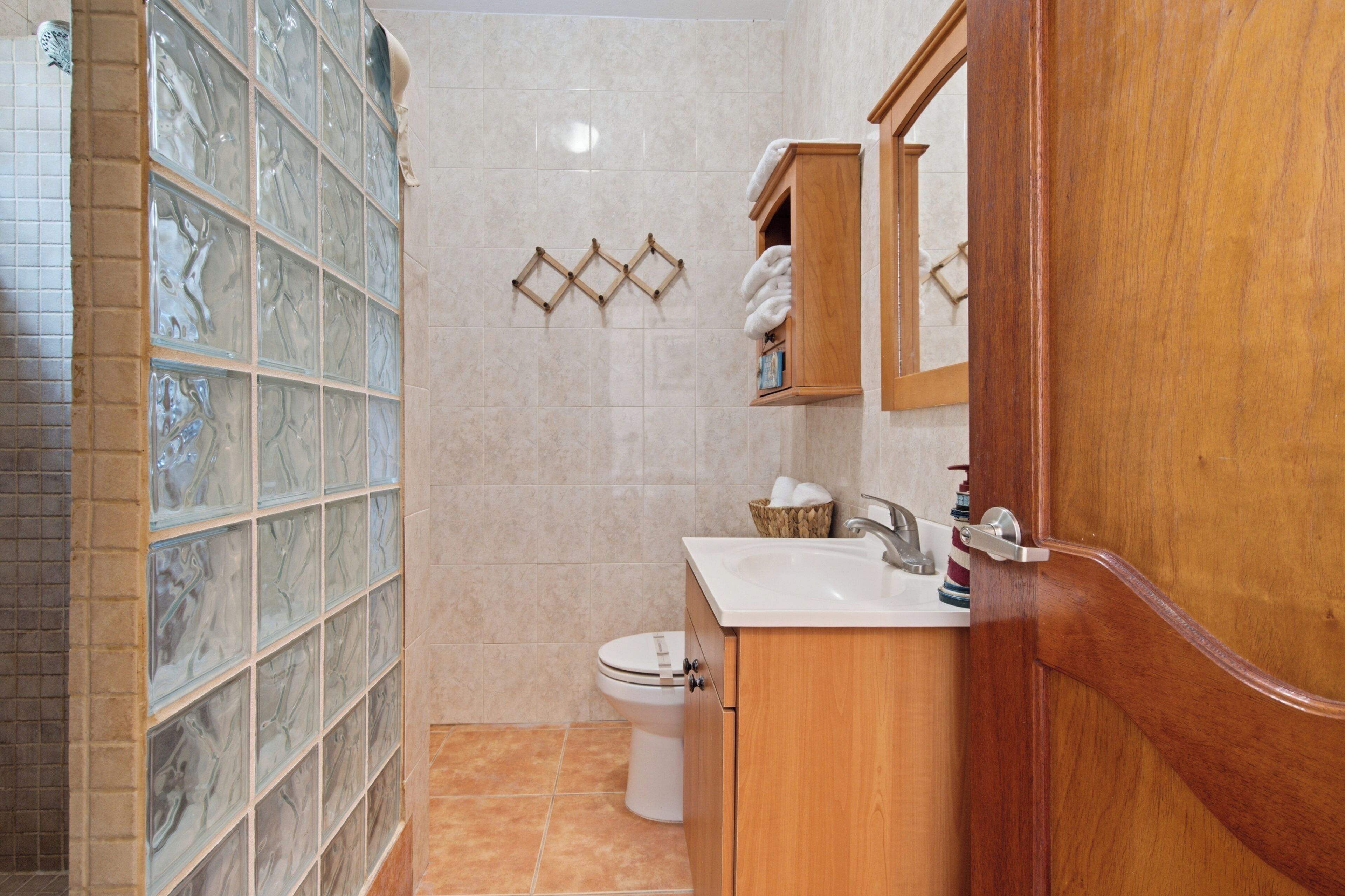 A bathroom with a glass shower enclosure, a toilet, a sink with a mirror, and a wooden cabinet.