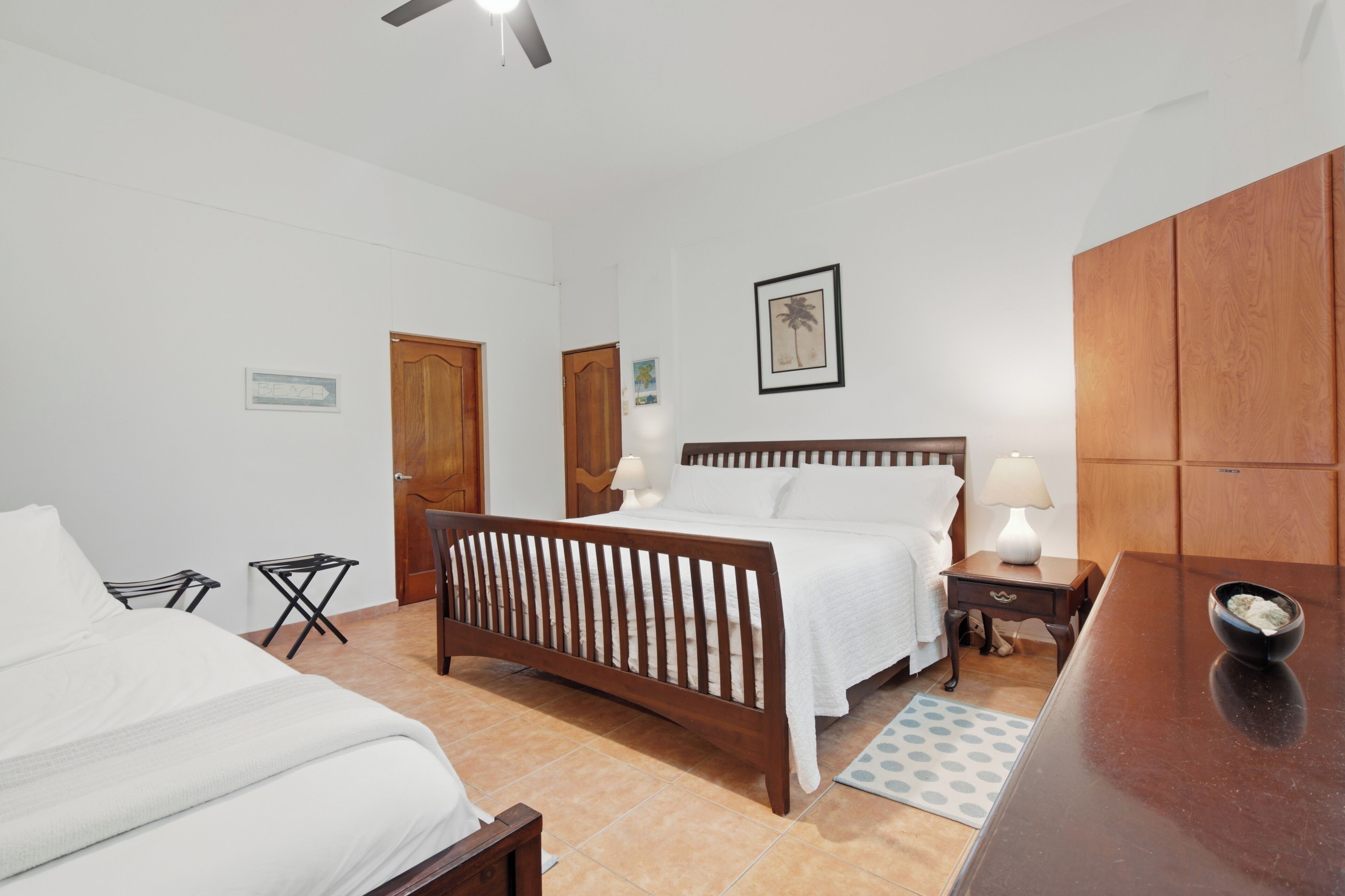 A bedroom with a wooden bed, a nightstand with a lamp, a small table, and a door.