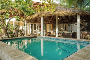 A pool area with a thatched roof structure, lounge chairs, and a clear blue pool. - Eco friendly beachfront oasis (Rincón)