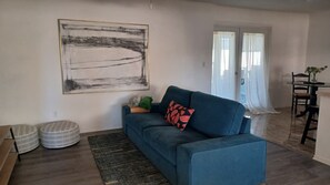 Ein Wohnzimmer mit blauem Sofa, einem großen abstrakten Gemälde und einem Essbereich mit Tisch und Stühlen.