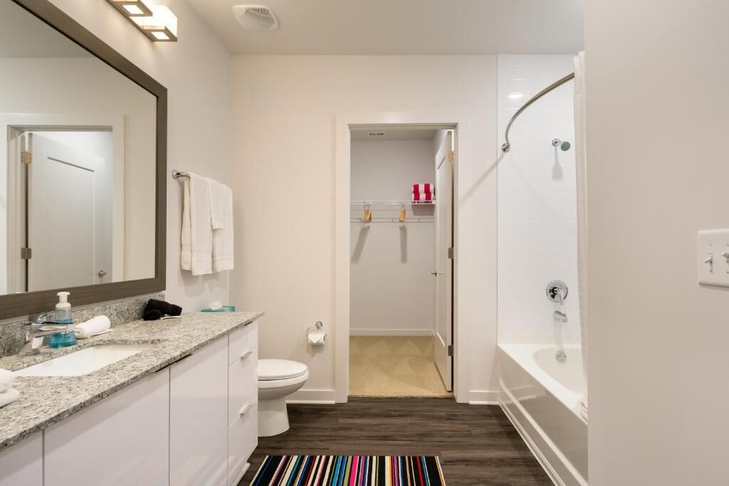 A modern bathroom with a large mirror, white fixtures, a shower, and a striped rug.