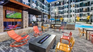 An outdoor lounge area with seating and a fire feature, surrounded by a pool and a multi-story building in the background. - BCA Spectacular Apartments (Atlanta)