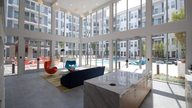 A spacious, modern interior with large windows, a marble island, and a pool visible outside. - BCA Spectacular Apartments (Atlanta)