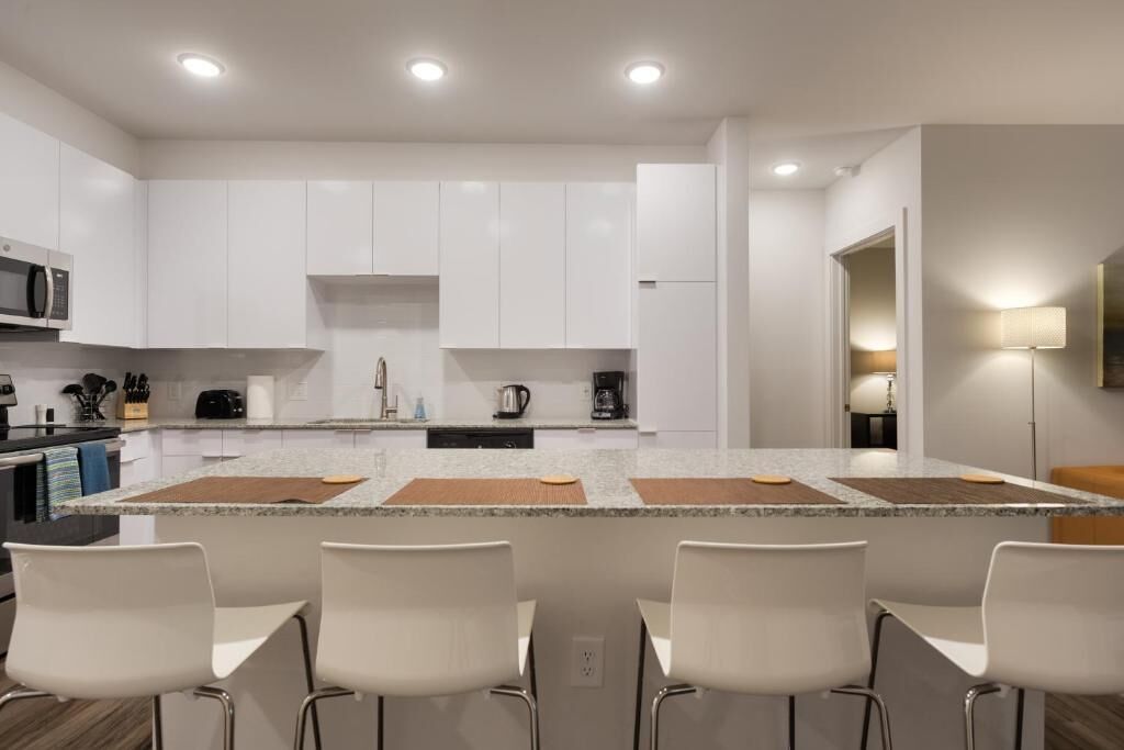 Une cuisine moderne avec des meubles blancs, un plan de travail en granit et un îlot central doté de tabourets de bar.