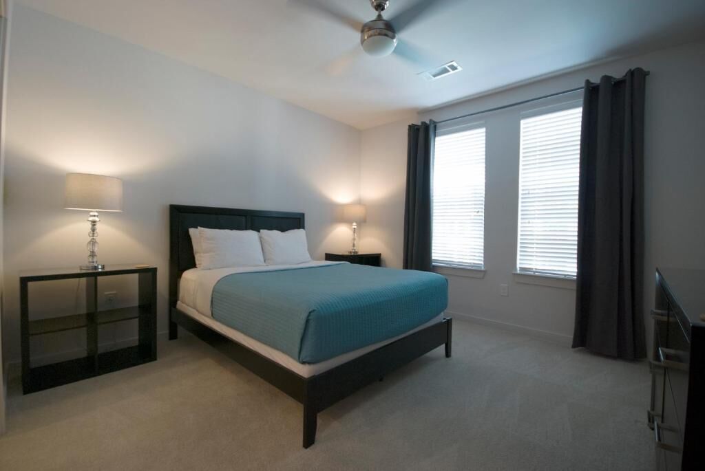 Une chambre à coucher comprenant un lit, deux tables de chevet, un ventilateur de plafond et une fenêtre avec des rideaux.