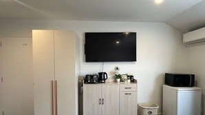 A compact hotel room with a bed, a wardrobe, a kitchenette, a TV, and a laundry basket. - Comfort stay Christchurch (Christchurch)