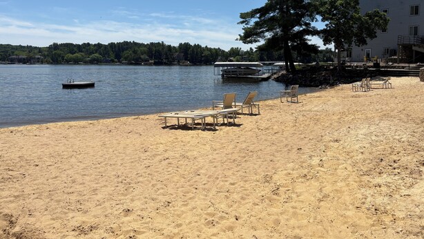 En sandstrand med liggestole, en mole og en bygning med balkon med udsigt over vandet.