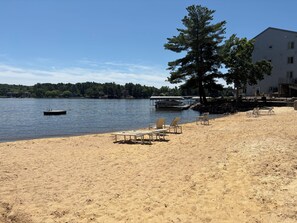 A sandy beach with lounge chairs, a dock, and a building with a dock. - Wisconsin Dells Getaway with Pools, Hot Tubs, Beach & Pickleball on Lake Delton (Wisconsin Dells)
