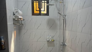 A small, modern bathroom with a shower, toilet, and bidet. It features marble tiles and a small window with a decorative frame. - Clover Homes Ug (Kampala)