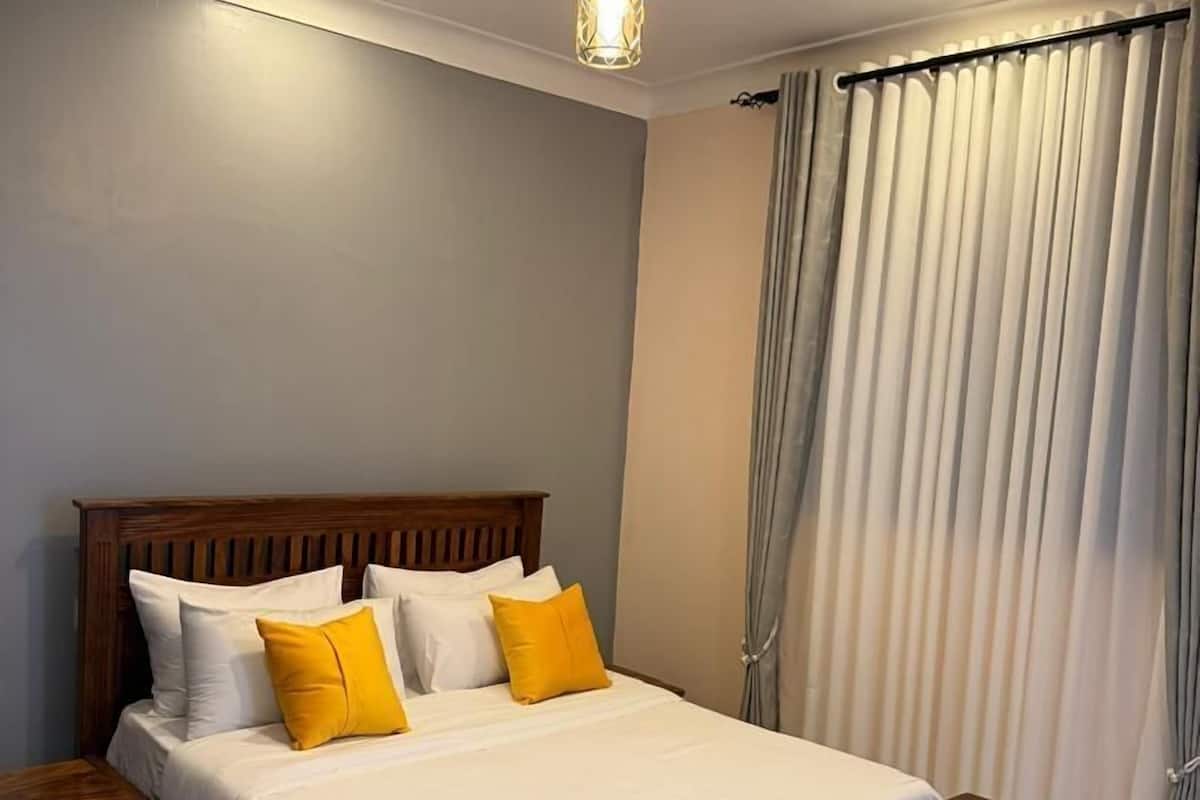 A bedroom with a wooden bed, white and yellow pillows, a nightstand, and a ceiling light.