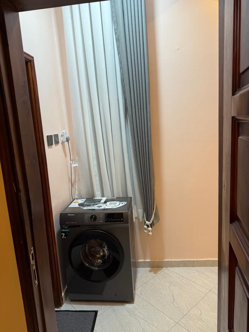 A laundry room with a washing machine, a power outlet, and a curtain.