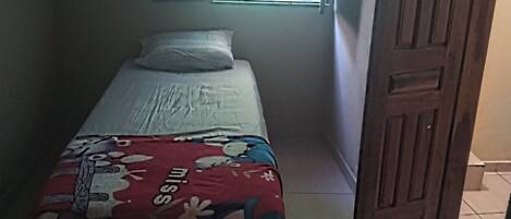 A small room with a single bed, a window, and a wooden door.